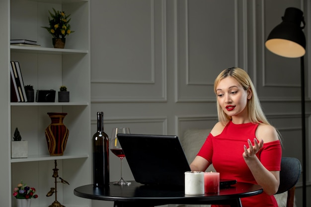 Ragazza bionda di amore virtuale in vestito rosso alla data di distanza con il vino che parla sulla macchina fotografica