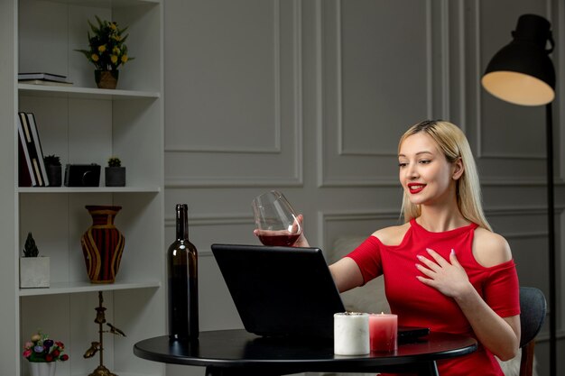 Virtual love cute blonde girl in red dress on distance date with wine cheering with glass