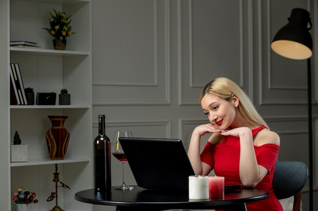 Виртуальная любовь милая блондинка в красном платье на дистанционном свидании с вином с руками на подбородке