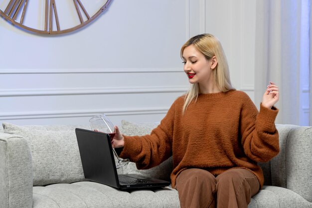 Virtual love cute young blonde girl in cozy sweater on distance computer date cheering with wine