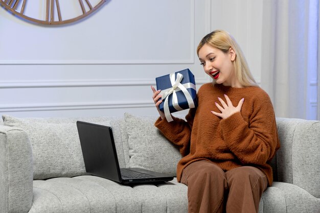 距離コンピュータの日付の居心地の良いセーターで仮想愛かわいい若いブロンドの女の子はgiftboxのために幸せです