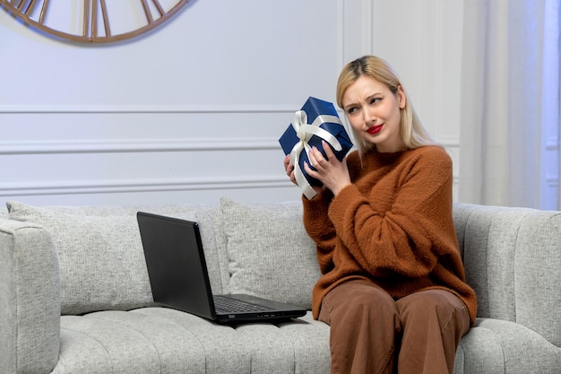 Amore virtuale ragazza bionda carina in maglione accogliente su data computer a distanza con confezione regalo