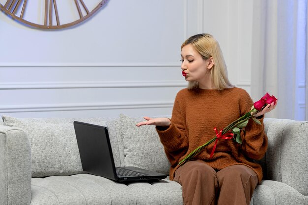 Virtual love cute young blonde girl in cozy sweater on distance computer date sending kisses