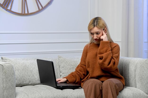 가상의 사랑스러운 젊은 금발 소녀는 아늑한 스웨터를 입고 사원을 만지는 컴퓨터 데이트를 하고 있습니다.