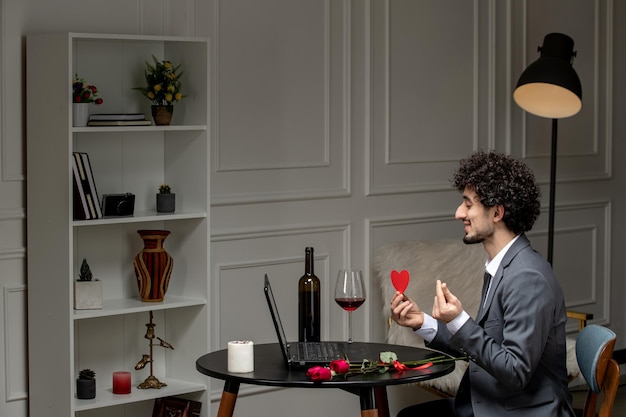 Virtual love handsome cute guy in suit with wine on a distance computer date holding finger hearts