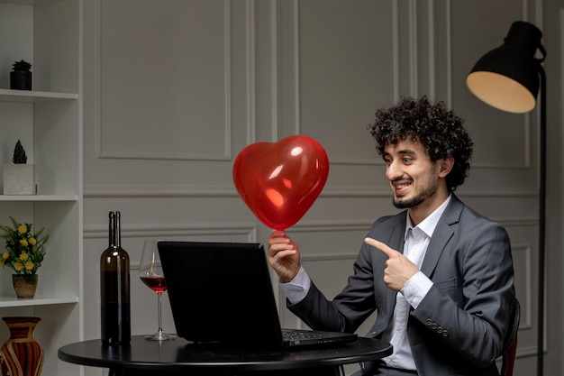 Virtual love handsome cute guy in suit with wine on a distance computer date pointing at balloon