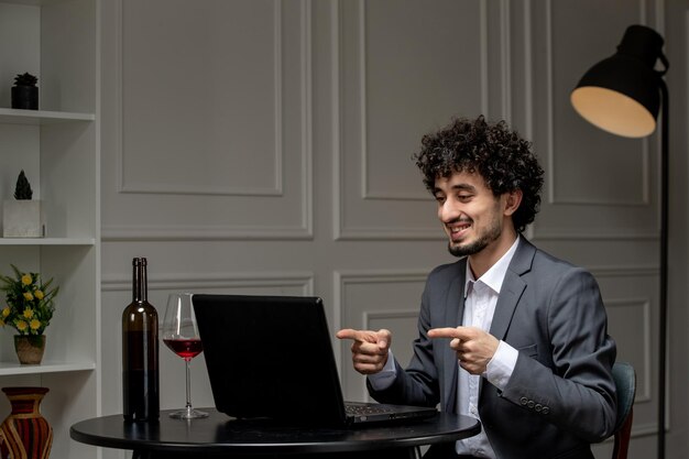 Virtual love handsome cute guy in suit with wine on a distance computer date pointing in camera