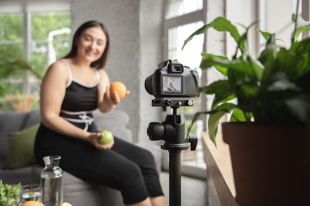 ビタミン。白人のブロガー、女性は、ダイエットと減量の方法をvlogで作成し、体をポジティブにし、健康的な食事をします。彼女のフルーツサラダの準備を記録するカメラを使用します。