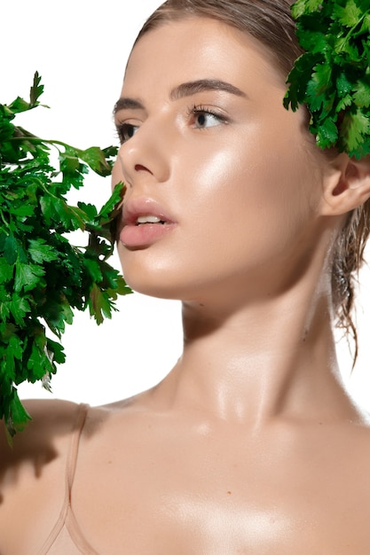 비타민. 흰색 위에 그녀의 얼굴에 녹색 잎을 가진 아름 다운 젊은 여자의 닫습니다.
