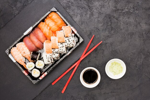 Vivid asian fish rolls on tray and chopsticks with soya sauce and wasabi over back concrete floor