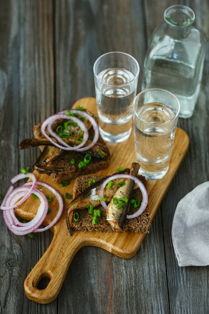 Vodka with fish and bread toast on wooden wall. Alcohol pure craft drink and traditional snacks. Negative space. Celebrating food and delicious. Top view.