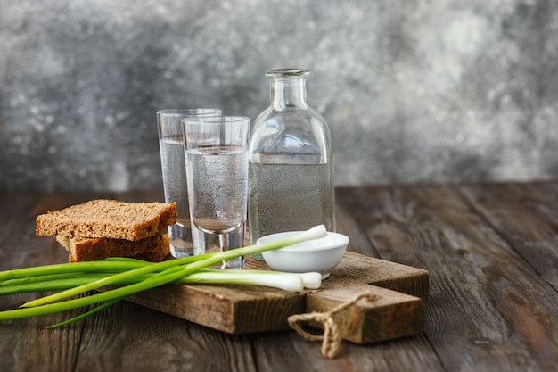 Vodka with green onion, bread toast and salt on wooden table