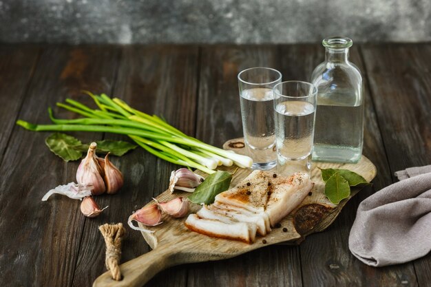 Vodka with lard and green onion on wooden table.