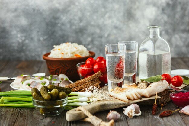 Водка с салом, соленой рыбой и овощами на деревянном столе