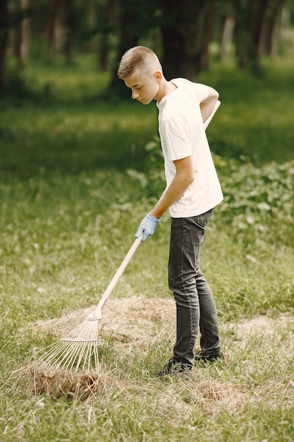 Volunteer teenager. European boy in gloves picking up plastic bottles into a black garbage bag outdoor. Volunteer and charity concept