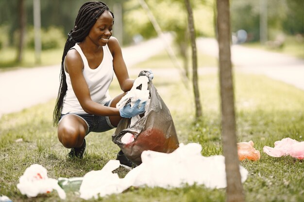자원봉사와 활동. 친환경적인 아프리카 소녀가 공원을 청소하고 있습니다. 그녀는 가방에 쓰레기를 넣고 있다.
