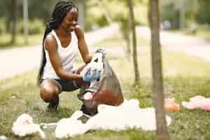 無料写真 ボランティア活動と行動主義。エコを意識したアフリカの女の子が公園を掃除しています。彼女はゴミを袋に入れています。