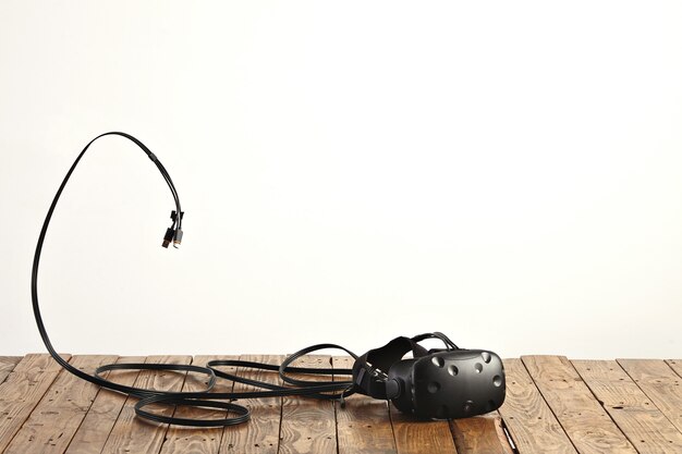 白い壁の粗い素朴な木製のテーブルにVRヘッドセットといくつかのコード