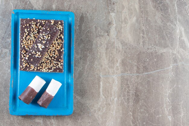 Waffle chocolate bar with nuts and candies on wooden plate on marble.