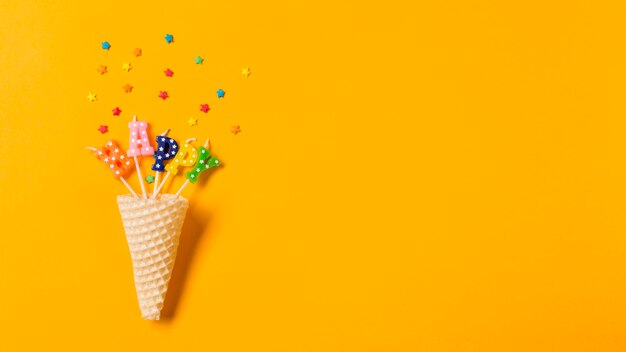 Waffle cone in the happy text candles with sprinkles on yellow backdrop