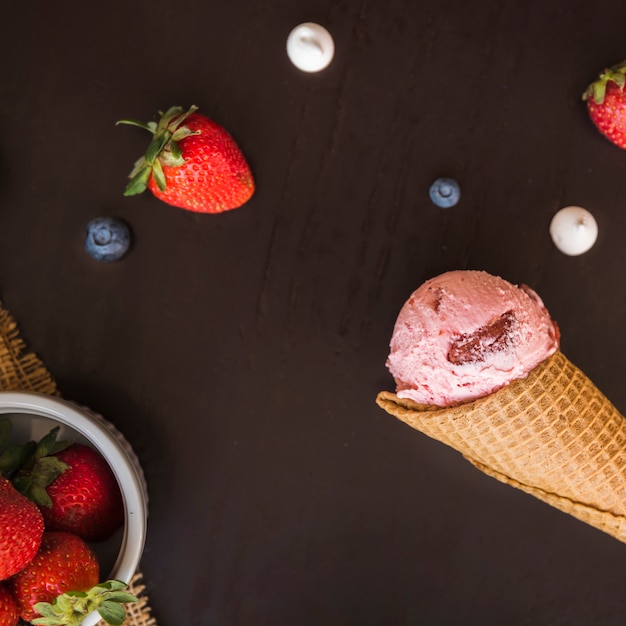 Waffle cone with ice cream near fresh berries in bowl