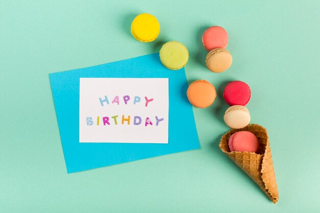 Waffle cone with macaroons near the happy birthday card on mint green backdrop