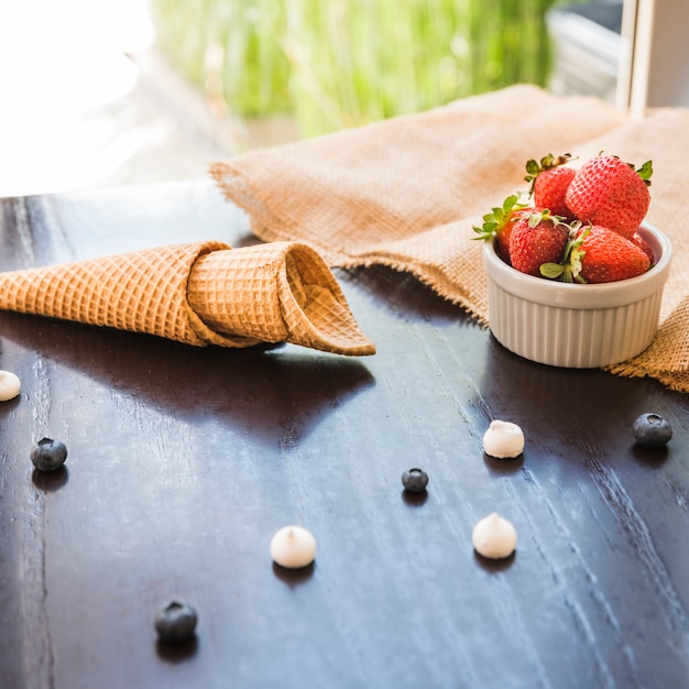 Waffle cones near fresh berries in bowl and napkin on table