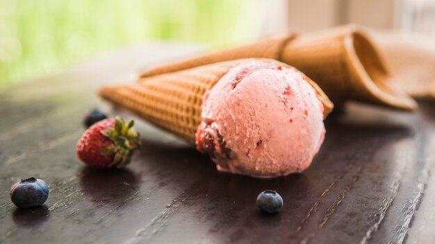 Waffle cones with ice cream near fresh berries on table