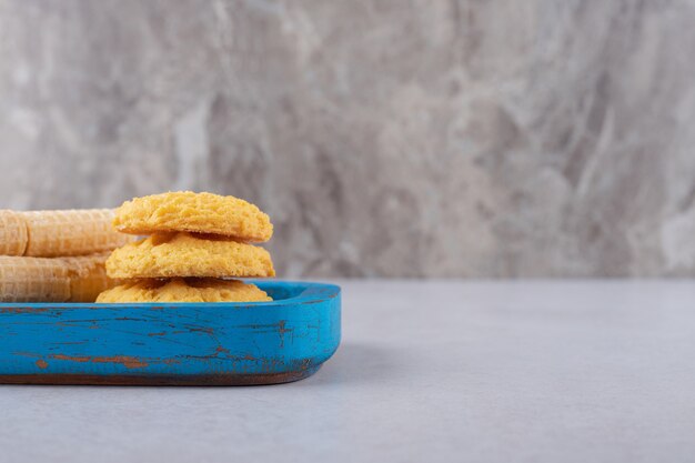 Waffle rolls and cookies on the wooden plate, the marble