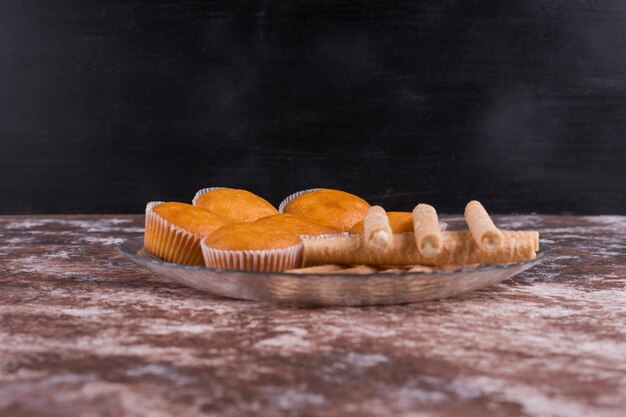 Waffle sticks and cupcakes in a glass platter on the marble on black wall