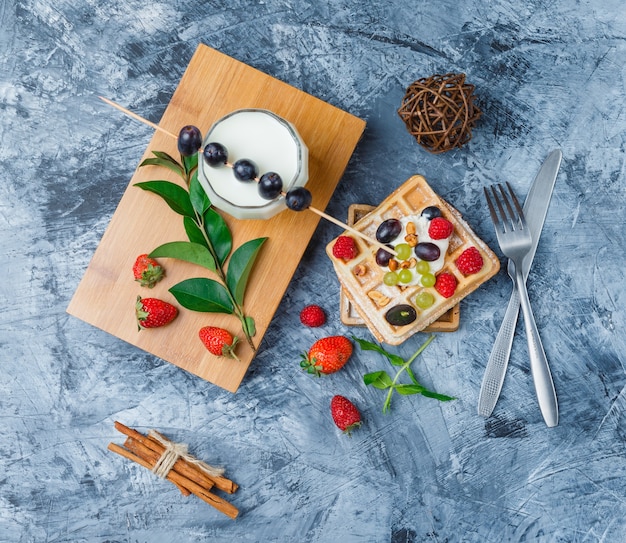 Waffles and fruits with milk, plums with sticks, cinnamon sticks and strawberries