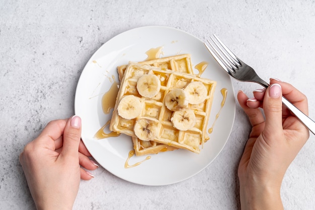 Foto gratuita waffle sul piatto con fettine di banana e forchetta tenuta mano