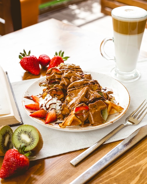 Waffles with chocolate sauce strawberry kiwi cream latte side view