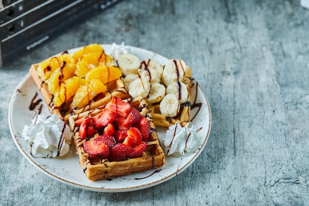 Waffles with ice-cream, banana, strawberry, chocolate in the white plate on the marble surface