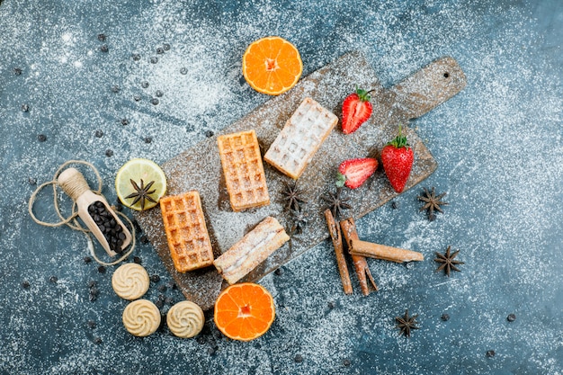 Waffles with spices, cookies, choco chips, fruits top view on grungy and cutting board surface