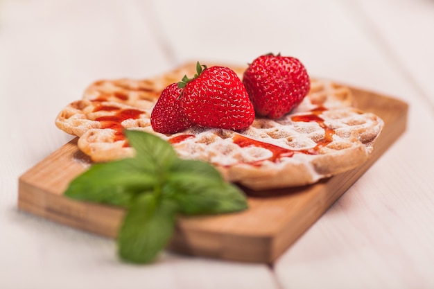 Waffles with strawberry on wooden plank