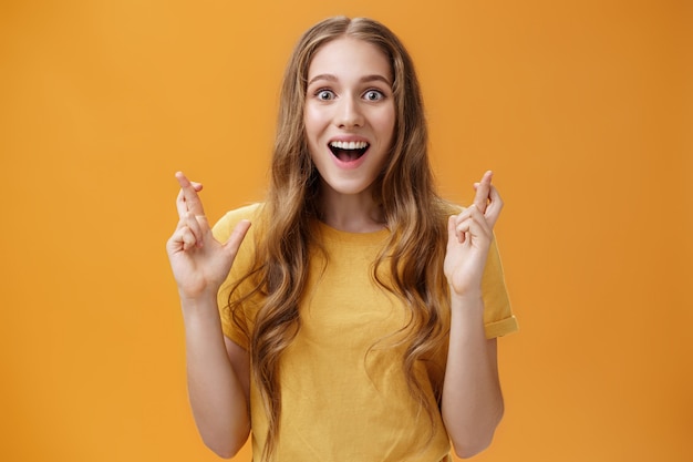 Free photo wais-up shot of interested amused and enthusiastic good-looking woman in casual t-shirt crossing fingers for good luck smiling amazed and delighted being happy and hopeful things will be well.