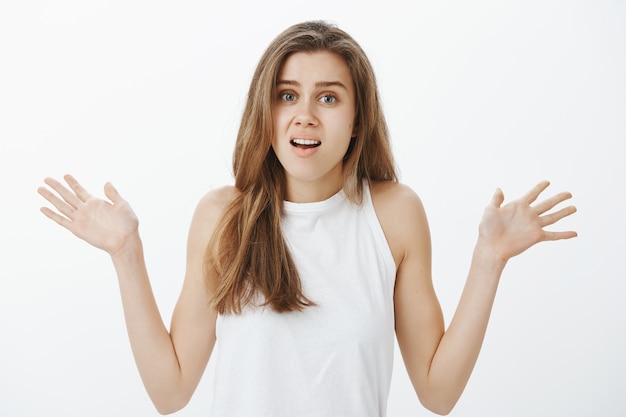 Waist-up of confused and worried young woman raising hands up indecisive