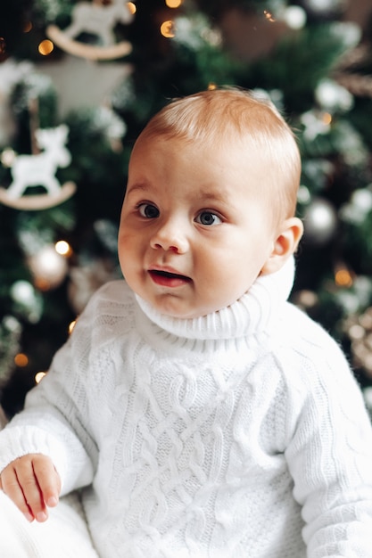 Waist-up photo of an adorable kid in knitted white sweater with Christmas tree