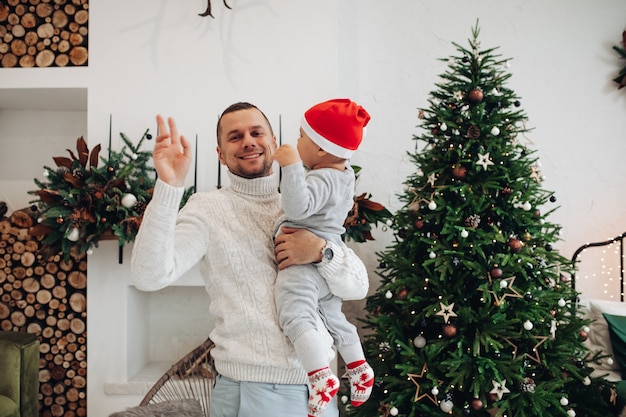크리스마스 트리 근처에 아이를 흔들며 들고 행복한 아빠의 허리 위로 사진