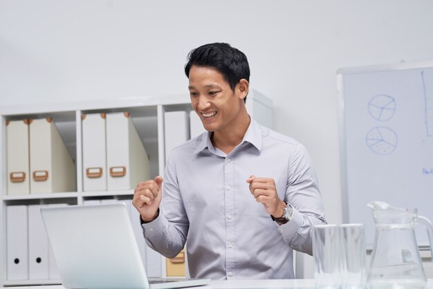 Waist up portrait of Asian businessman sitting at office desk looking at laptop screen 