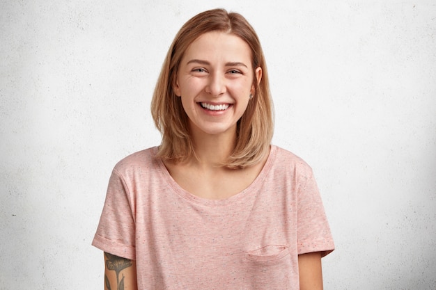 waist up portrait of cheerful lovely blue eyed female with bobbed hairstyle, expresses happiness, being delighted after unforgettable night with lover, isolated over white