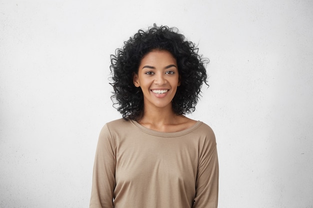 Waist up portrait of cheerful young mixed race female with curly hair posing in studio with happy smile