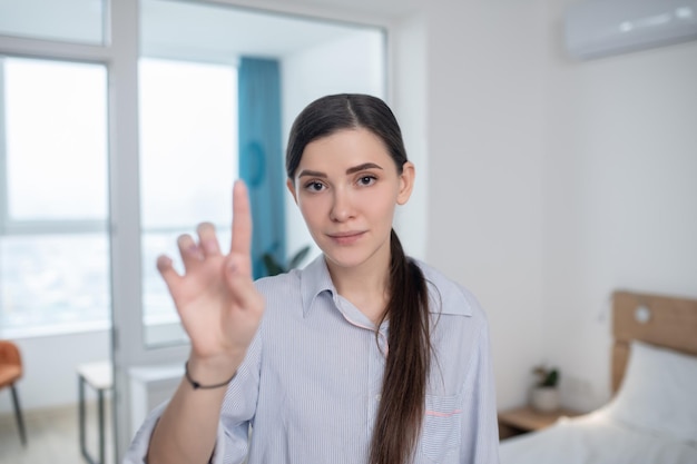 カメラに向かってポーズをとっている人差し指を上げたかわいい静かな女性のウエストアップの肖像画