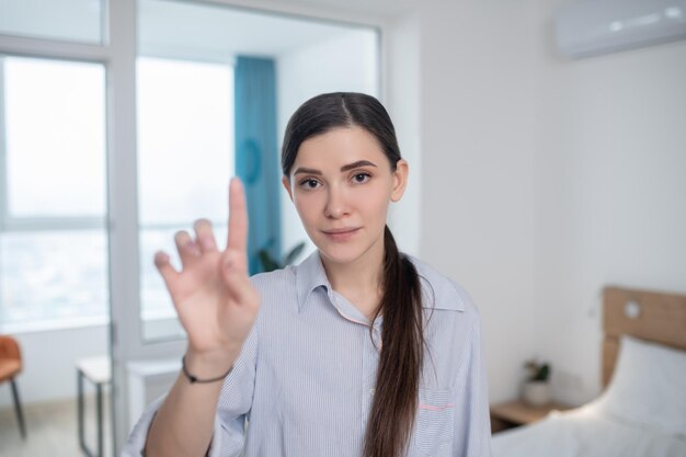 Waist-up portrait of a cute tranquil woman with a raised index finger posing for the camera