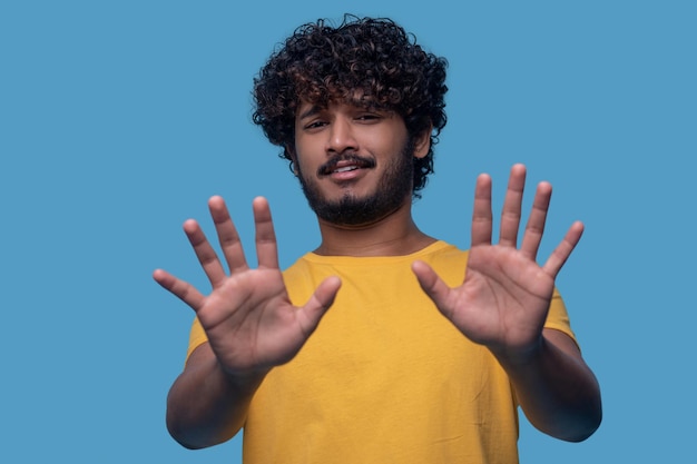 Waist-up portrait of a displeased young man holding two hands with fingers splayed before him