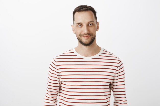 Waist-up portrait of happy calm guy with beard in striped pullover smiling broadly