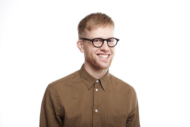 Waist up portrait of happy ecstatic young man with stubble wearing trendy glasses and formal shirt grinning broadly, feeling overjoyed after he got promotion at work and bonus for excellent job