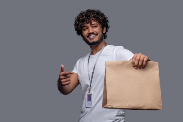 Waist-up portrait of a male with an ID badge pointing his forefinger at the package in his hand