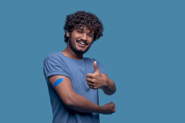 Free photo waist-up portrait of a pleased man with the adhesive plaster on his arm making a thumbs-up gesture